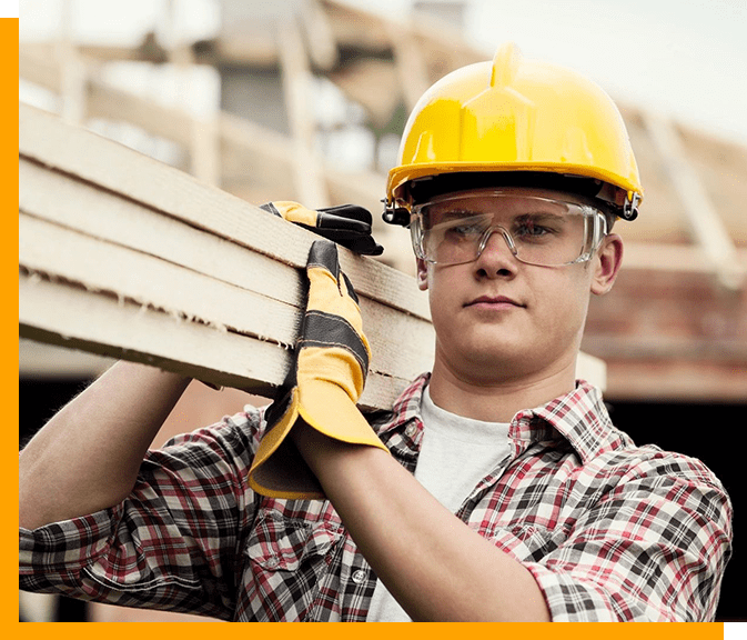 A man in hard hat holding wood on his shoulder.