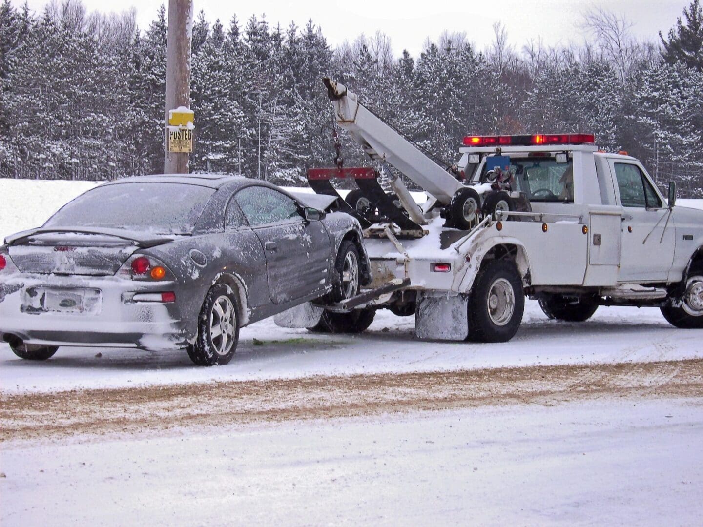 A tow truck towing a car on the side of a road.