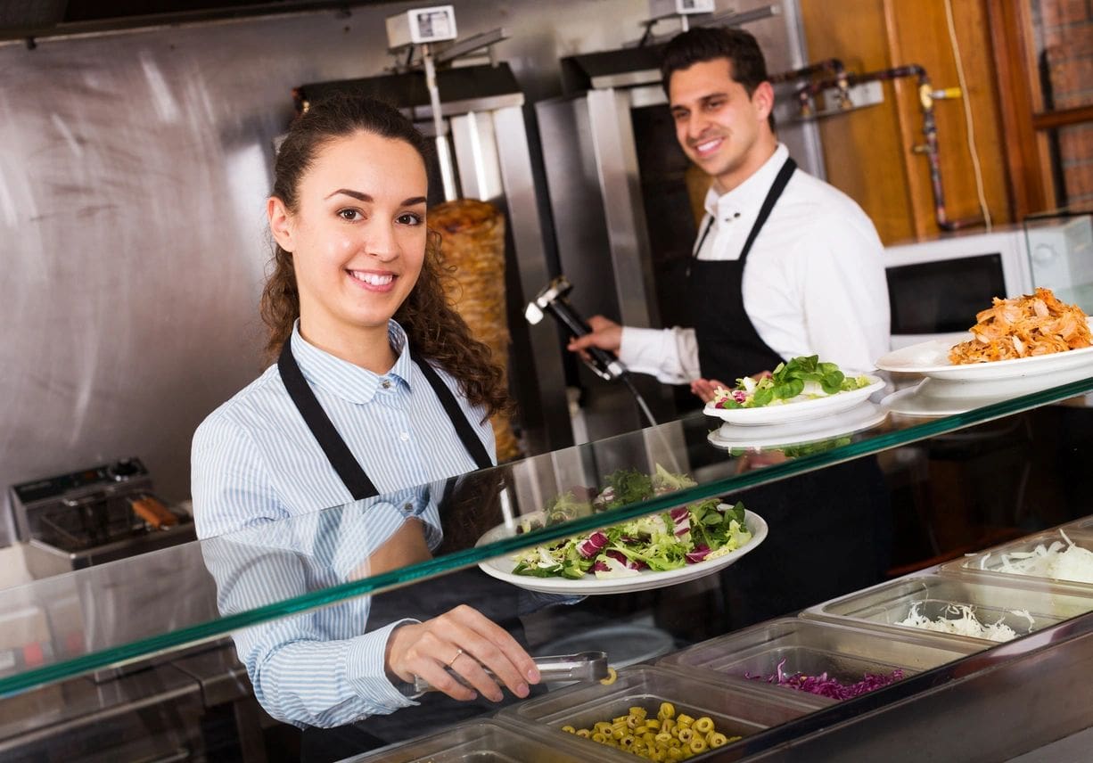 Two people in a kitchen preparing food for service.