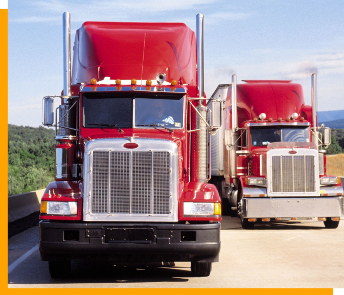 Two red trucks are driving down the road.