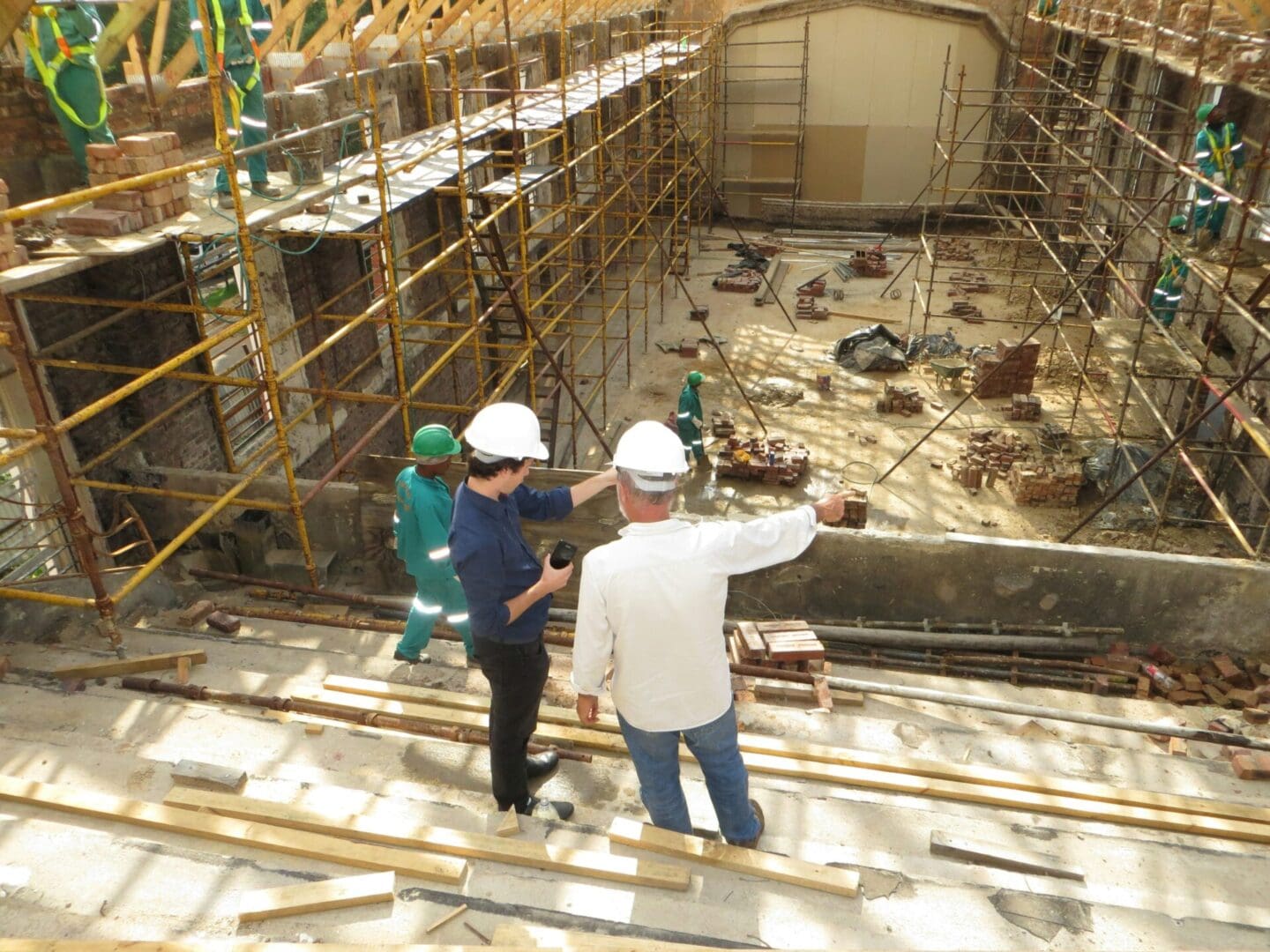 Two men in hard hats and a woman wearing white are standing on scaffolding.