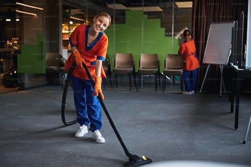 A woman in an orange shirt is using a vacuum